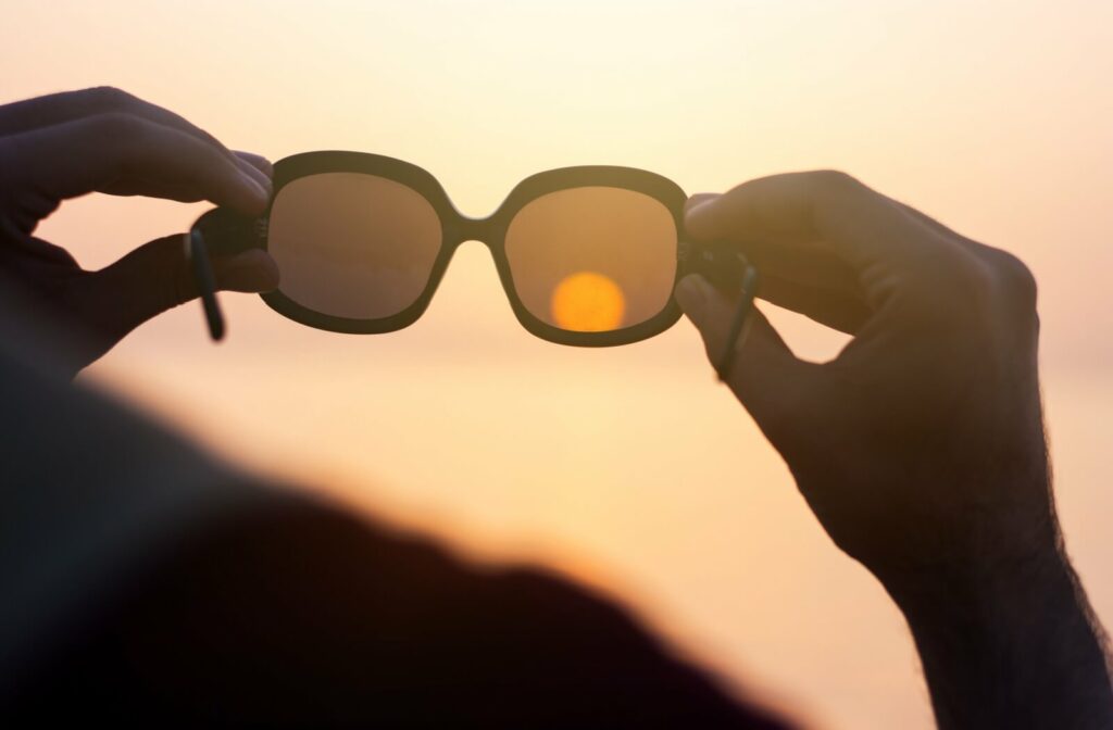 Person holding up sunglasses toward the light to check if the lenses are polarized.